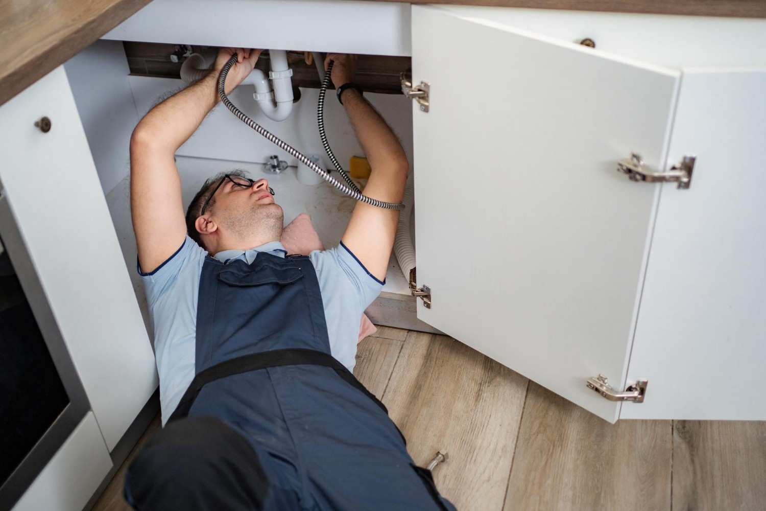 plumber fixing a leaking pipe under a sink